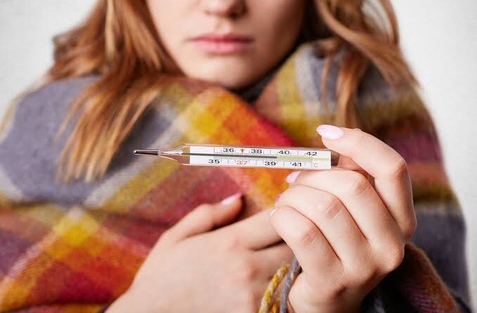 Mujer con fiebre y termómetro en mano