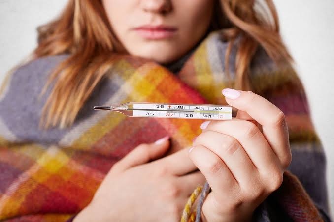 Mujer con fiebre y termómetro en mano